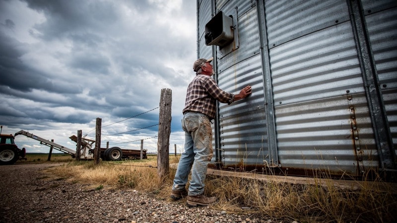 Farmer inspecting tall grain bin on a cloudy prairie day